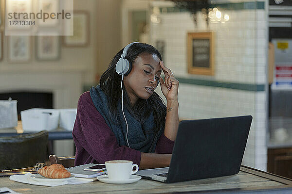 Müde junge Geschäftsfrau mit Kopfhörer arbeiten am Laptop im Café