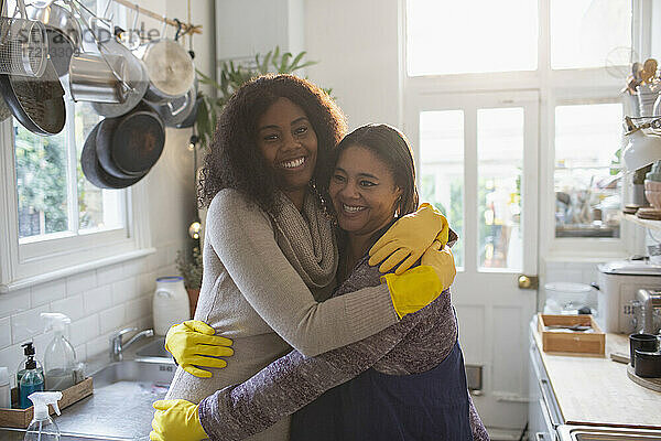 Porträt glückliche Mutter und Tochter in Gummihandschuhen umarmen in der Küche