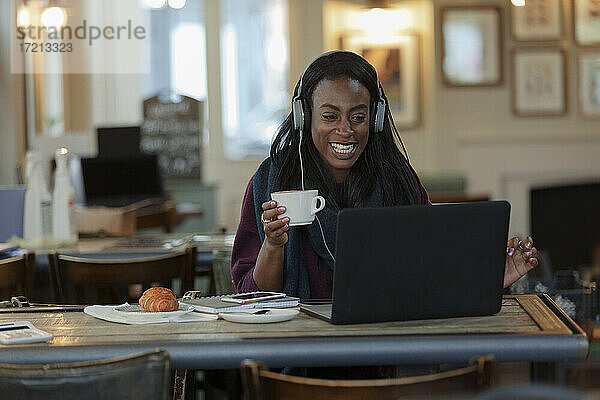 Frau mit Kopfhörer trinken Kaffee und arbeiten am Laptop im Café