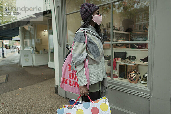 Junge Frau mit Gesichtsmaske und Einkaufstüten vor einem Geschäft