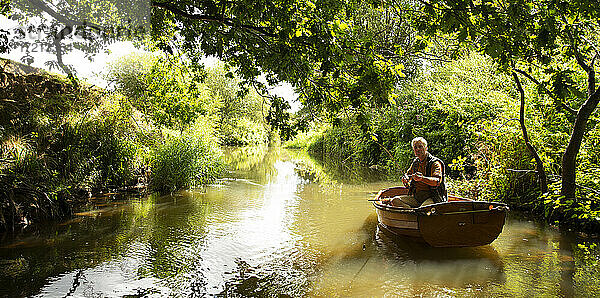 Mann Fliegenfischen vom Boot auf ruhigen grünen Fluss