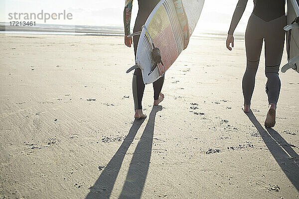 Weibliche Surfer tragen Surfbretter am sonnigen Sandstrand