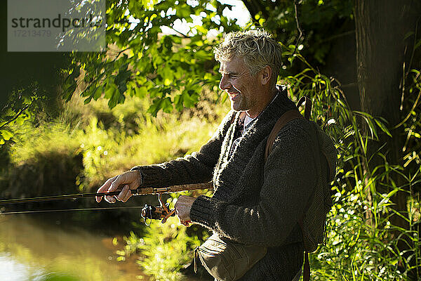 Glücklicher Mann Fliegenfischen am sonnigen Flussufer