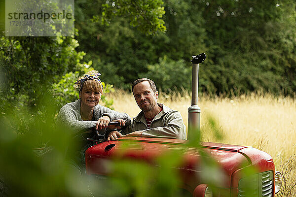 Portrait glückliches Paar am Traktor im Obstgarten
