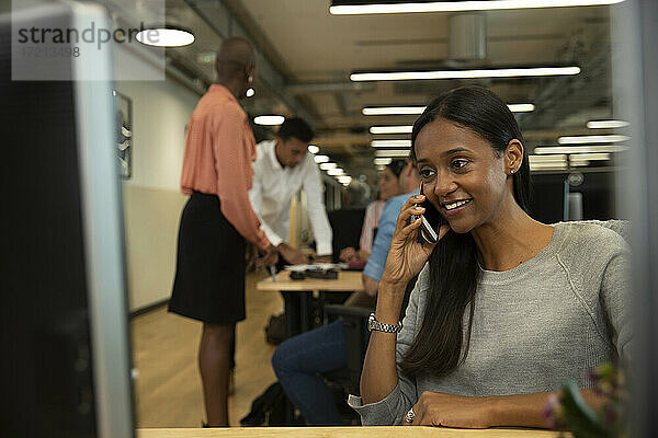 Lächelnde Geschäftsfrau spricht auf Smartphone in Großraumbüro