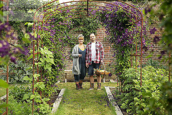 Porträt glückliches Paar ernten Gemüse unter Blume Spalier
