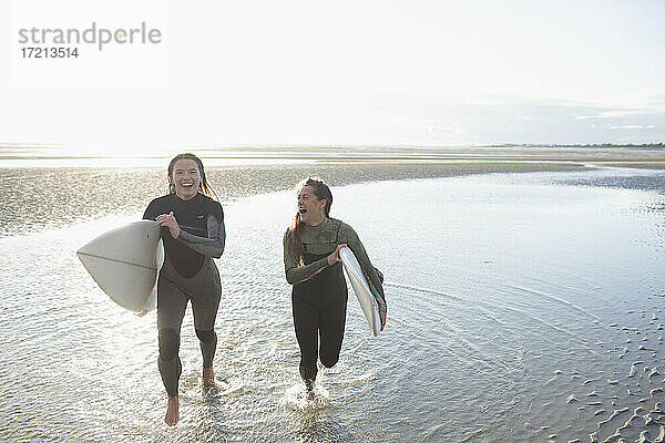 Sorglose junge Surferinnen laufen mit Surfbrettern im sonnigen Ozean