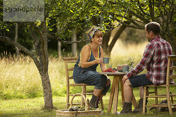 Ehepaar macht eine Pause von der Gartenarbeit am Tisch im Obstgarten