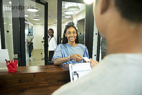 Glückliche Geschäftsfrau mit Ausweis beim Einchecken am Büroempfang