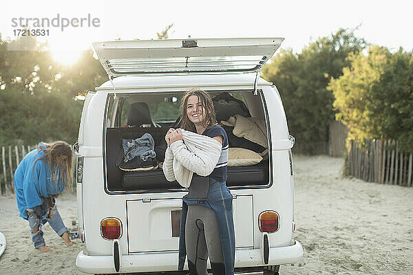 Porträt junge weibliche Surferin beim Anziehen des Pullovers am sonnigen Wohnmobil