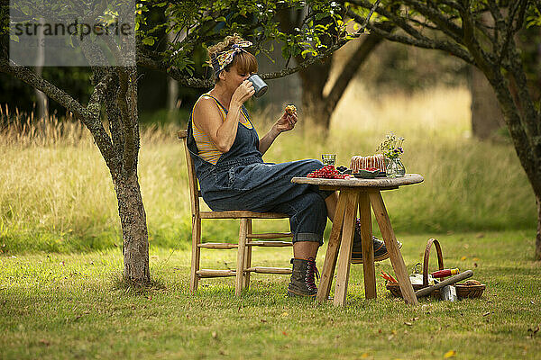 Frau macht Pause von der Gartenarbeit und isst Kuchen am Gartentisch