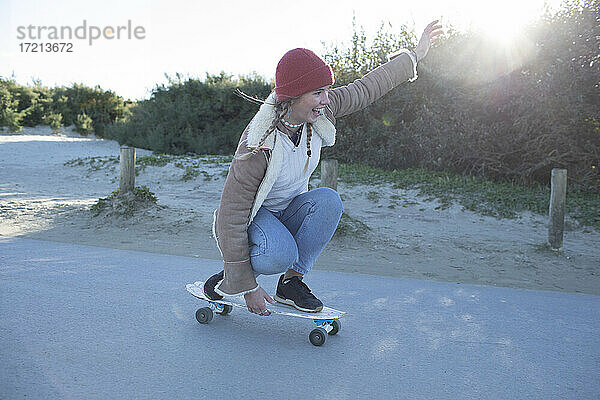 Unbekümmerte junge Frau beim Skateboarden auf dem Strandweg