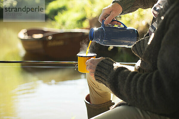 Mann Fliegenfischen und gießen Kaffee am sonnigen Fluss