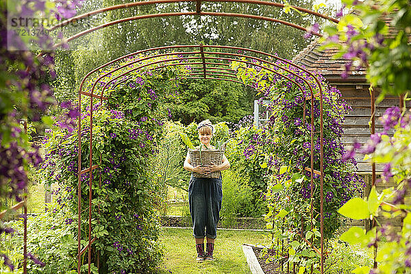 Porträt Frau mit Korb unter Spalier mit lila Blumen im Garten