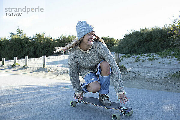 Unbekümmerte junge Frau beim Skateboarden auf dem Strandweg