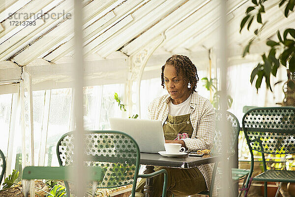 Weibliche Gartenladenbesitzerin arbeitet am Laptop im Gewächshaus