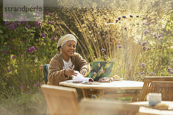 Frau arbeitet am Laptop am idyllischen Gartencafé Tisch