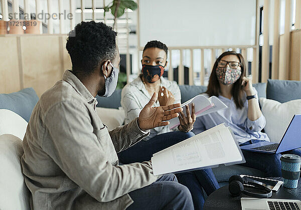 Geschäftsleute mit Gesichtsmasken  die auf einem Bürosofa Papierkram diskutieren