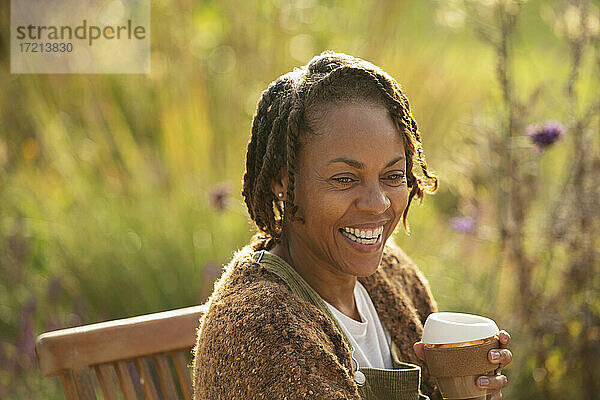 Glückliche Frau mit Kaffee lachend auf der sonnigen Gartenterrasse