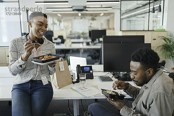 Glückliche Geschäftsleute essen Takeout Mittagessen am Schreibtisch im Großraumbüro