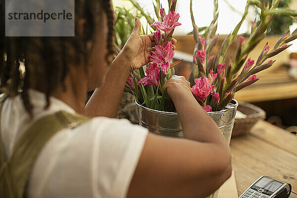 Weibliche Floristin arrangiert rosa Blumen in Eimer im Laden