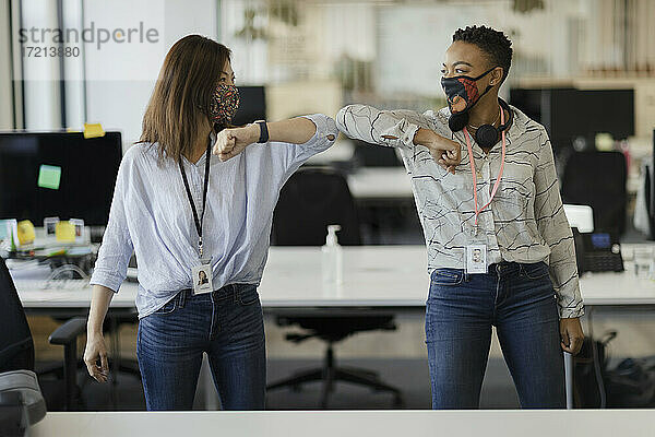 Geschäftsfrauen mit Gesichtsmasken Ellbogenstöße im Büro