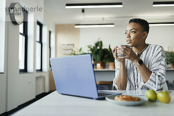 Nachdenkliche junge Geschäftsfrau trinkt Kaffee am Laptop im Büro