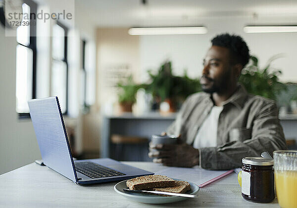 Nachdenklicher Geschäftsmann trinkt Kaffee am Laptop im Büro