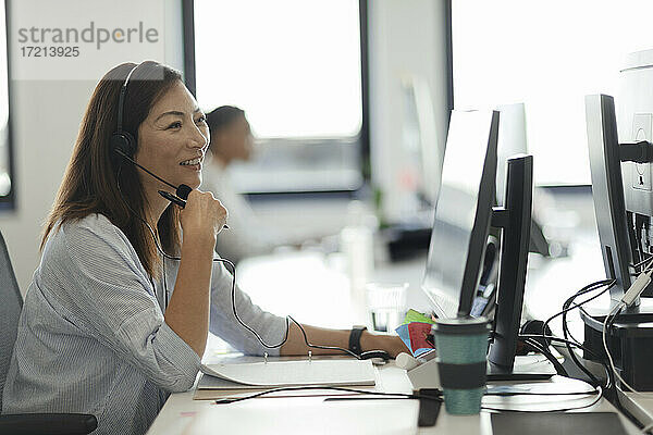 Lächelnde Geschäftsfrau mit Headset arbeitet am Computer im Büro