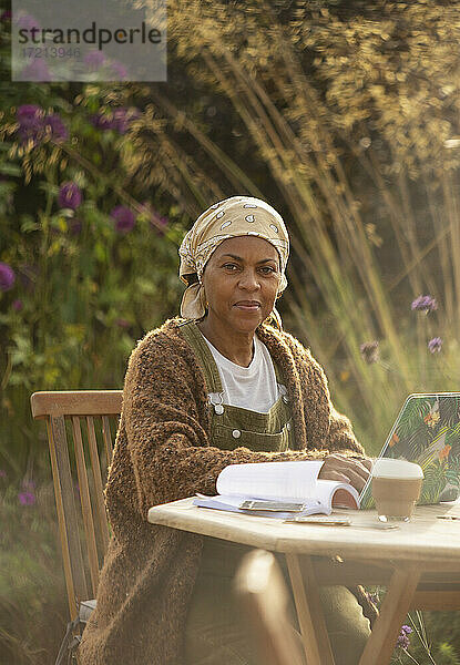 Porträt selbstbewusste Frau  die am Laptop auf dem Gartenterrassentisch arbeitet