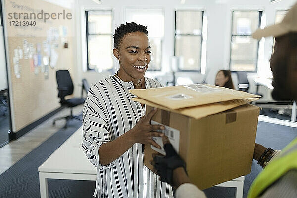Glückliche Geschäftsfrau empfängt Pakete von Kurier im Büro