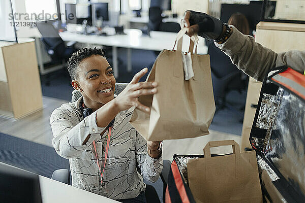 Glückliche Geschäftsfrau empfängt Mittagessen Tasche von Kurier im Büro
