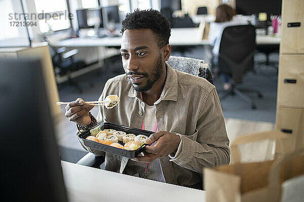 Geschäftsmann isst Sushi Takeout Mittagessen am Computer im Büro