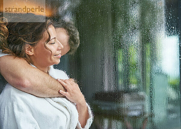 Zärtliches romantisches Paar  das sich am regnerischen Fenster umarmt