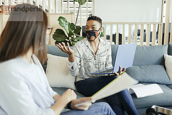 Geschäftsfrauen mit Gesichtsmasken treffen sich auf dem Bürosofa