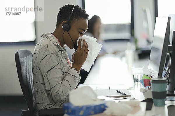 Geschäftsfrau in Headset schnäuzt Nase in Taschentuch im Büro Schreibtisch