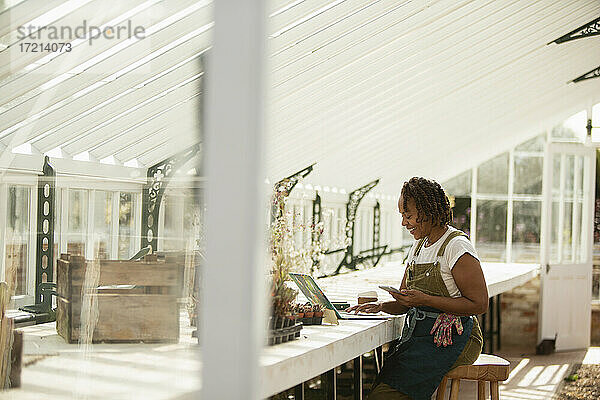 Weibliche Gartenladenbesitzerin arbeitet am Laptop im Gewächshaus
