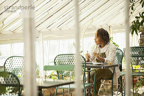 Weibliche Gartenladenbesitzerin trinkt Tee am Tisch im Gewächshaus