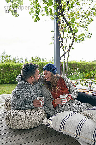 Zärtliches Paar entspannt mit Kaffee auf Kissen auf der Terrasse