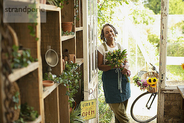 Porträt glückliche weibliche Blumenhändlerin mit Blumenstrauß in der Ladentür