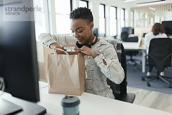 Geschäftsfrau öffnet Takeout-Lunchbag am Schreibtisch im Büro