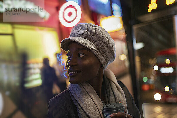 Junge Frau mit Hut auf dem Bürgersteig der Stadt bei Nacht