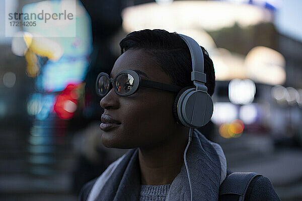 Selbstbewusste stilvolle junge Frau mit Kopfhörer auf städtischen Straße
