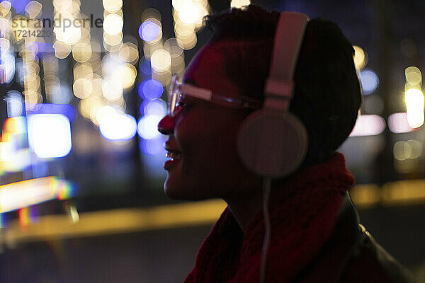 Junge Frau mit Kopfhörer in der Stadt mit Lichtern in der Nacht