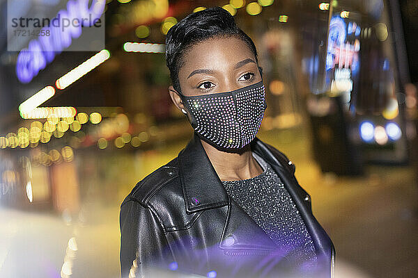 Junge Frau in funkelnden Maske in der Stadt mit Lichtern in der Nacht