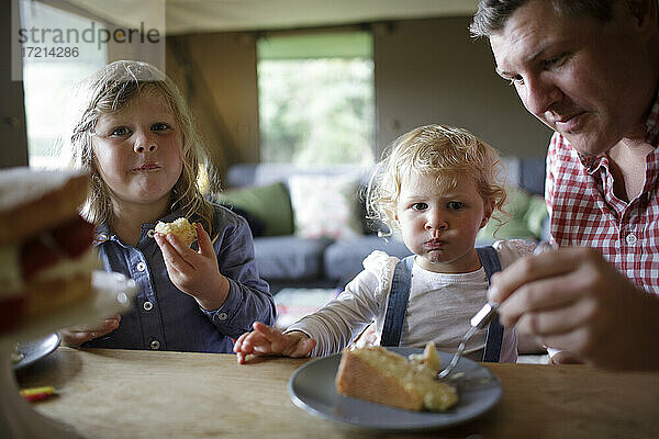 Vater und Töchter essen Kuchen am Esstisch