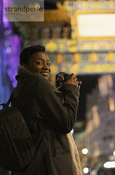 Porträt glückliche junge Frau mit Kamera in der Stadt bei Nacht