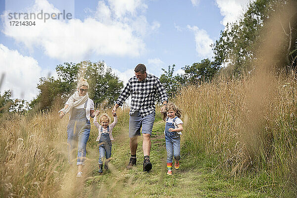 Glückliche Familie hält Hände laufen in sonnigen ländlichen Feld