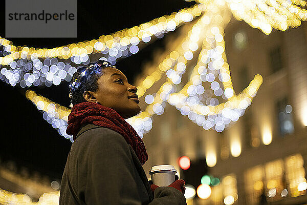 Serene junge Frau mit Kaffee in der Stadt mit Lichtern in der Nacht