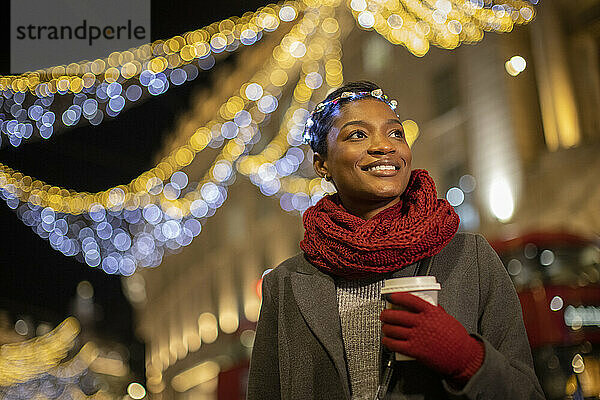Glückliche junge Frau mit Weihnachtslicht Stirnband in der Stadt in der Nacht